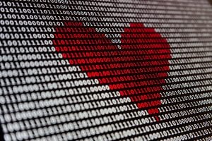 Computer screen showing binary code in white with some in red in the shape of a heart; image by Alexander Sinn, via Unsplash.com.