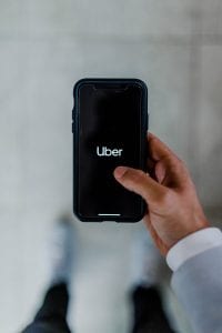 Man with black smartphone with “Uber” on the screen; image by Austin Distel, via Unsplash.com