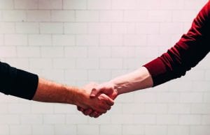 Two men shaking hands in front of a white tiled wall; image by Chris Liverani, via Unsplash.com.