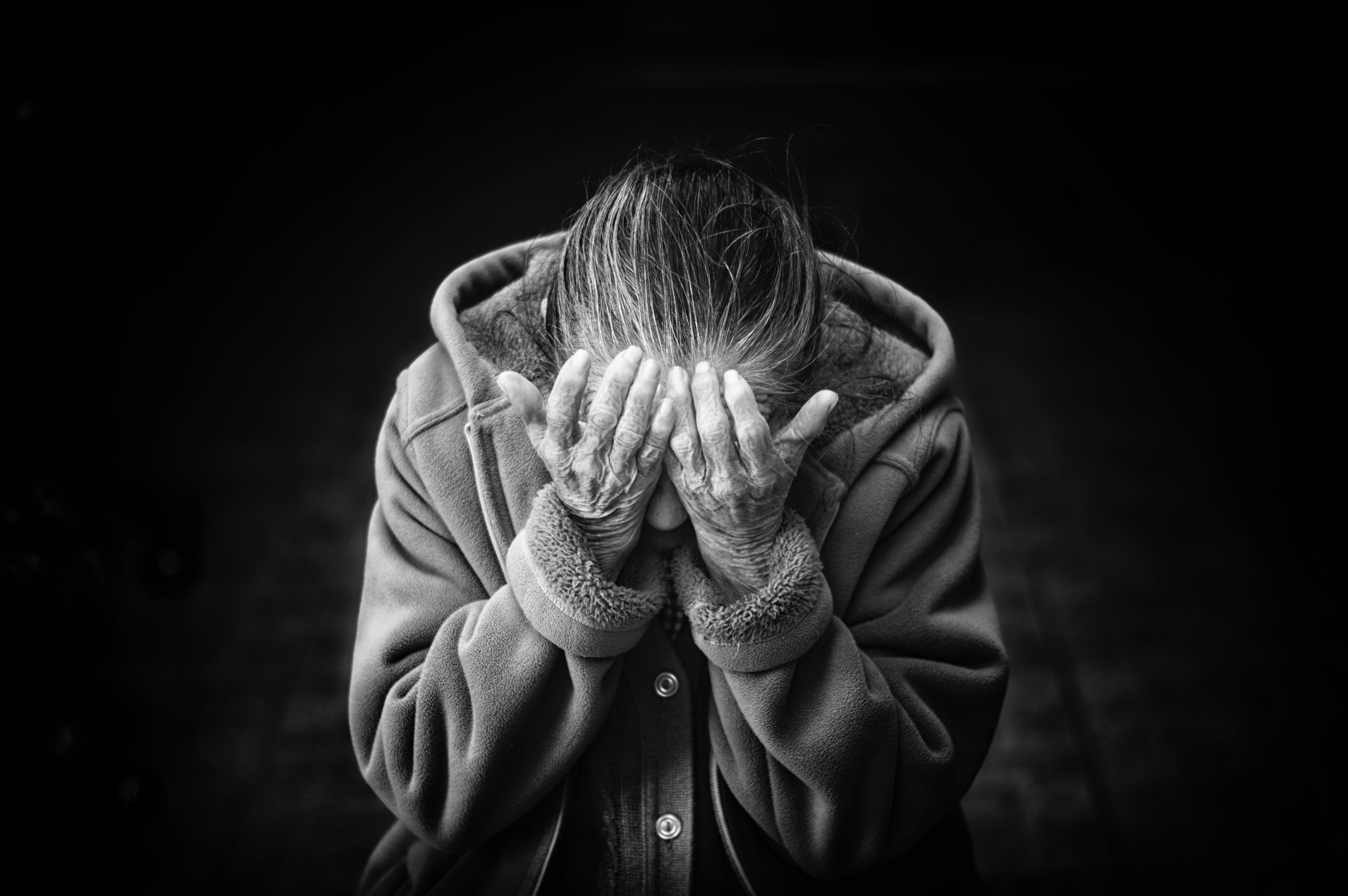 Elderly woman covering her face; image by Cristian Newman, via Unsplash.com.