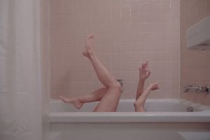 Woman’s arms and legs protruding from white bathtub as she is on her back; image by Julieta Christy, via Unsplash.com.