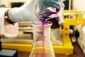 Person pouring purple liquid in clear glass container; image by Louis Reed, via Unsplash.com.