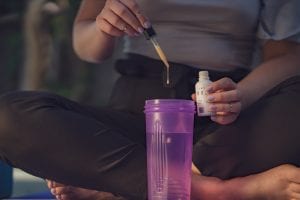 Woman mixing her water-soluble CBD from Eir Health with water in a purple shaker; image by Michal Wozniak, via Unsplash.com.