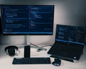 Computer monitor, keyboard, mouse and laptop on a desk; image by Pakata Goh, via Unsplash.com.