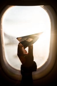 Child holding paper airplane in front of an airplane window; image by Sebastián León Prado, via Unsplash.com.