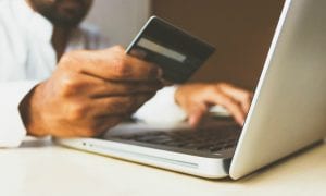 Man holding credit card while using laptop; image by rupixen.com, via Unsplash.com.