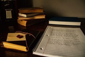 Books and a spiral-bound notebook of notes on a desk; image by Chloestrong, via Pixabay.com.