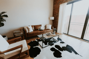 Living room, with cow patterned rug and brown leather sofa; image by Hannah Busing, via Unsplash.com.