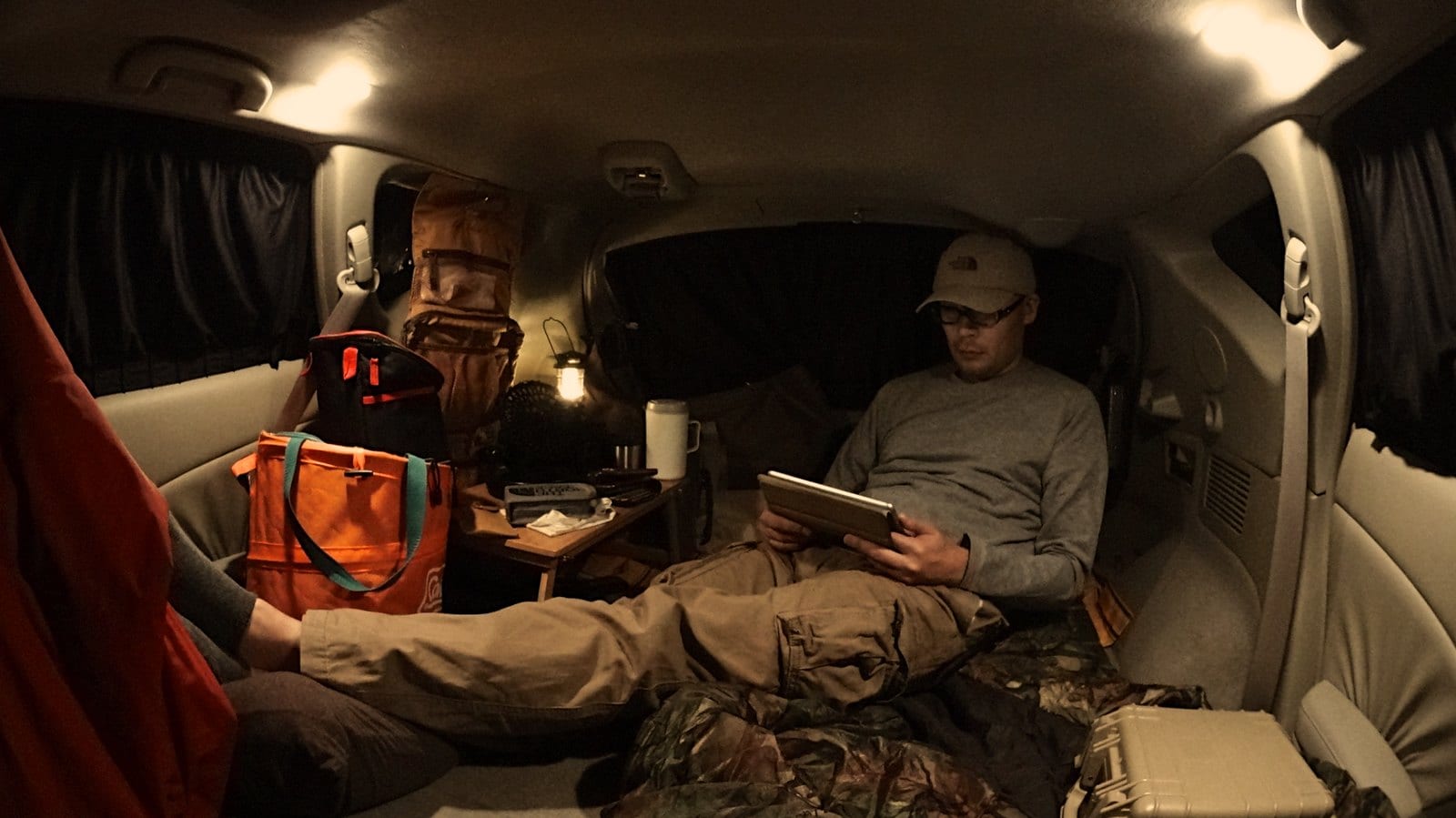 A young Asian man reclines while using an e-book reader in a comfortably furnished SUV.