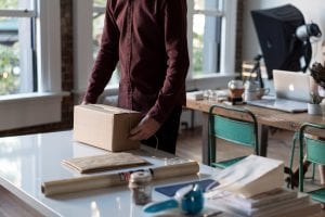 Man in maroon shirt packing a box in the office; image by Bench Accounting, via Unsplash.com.