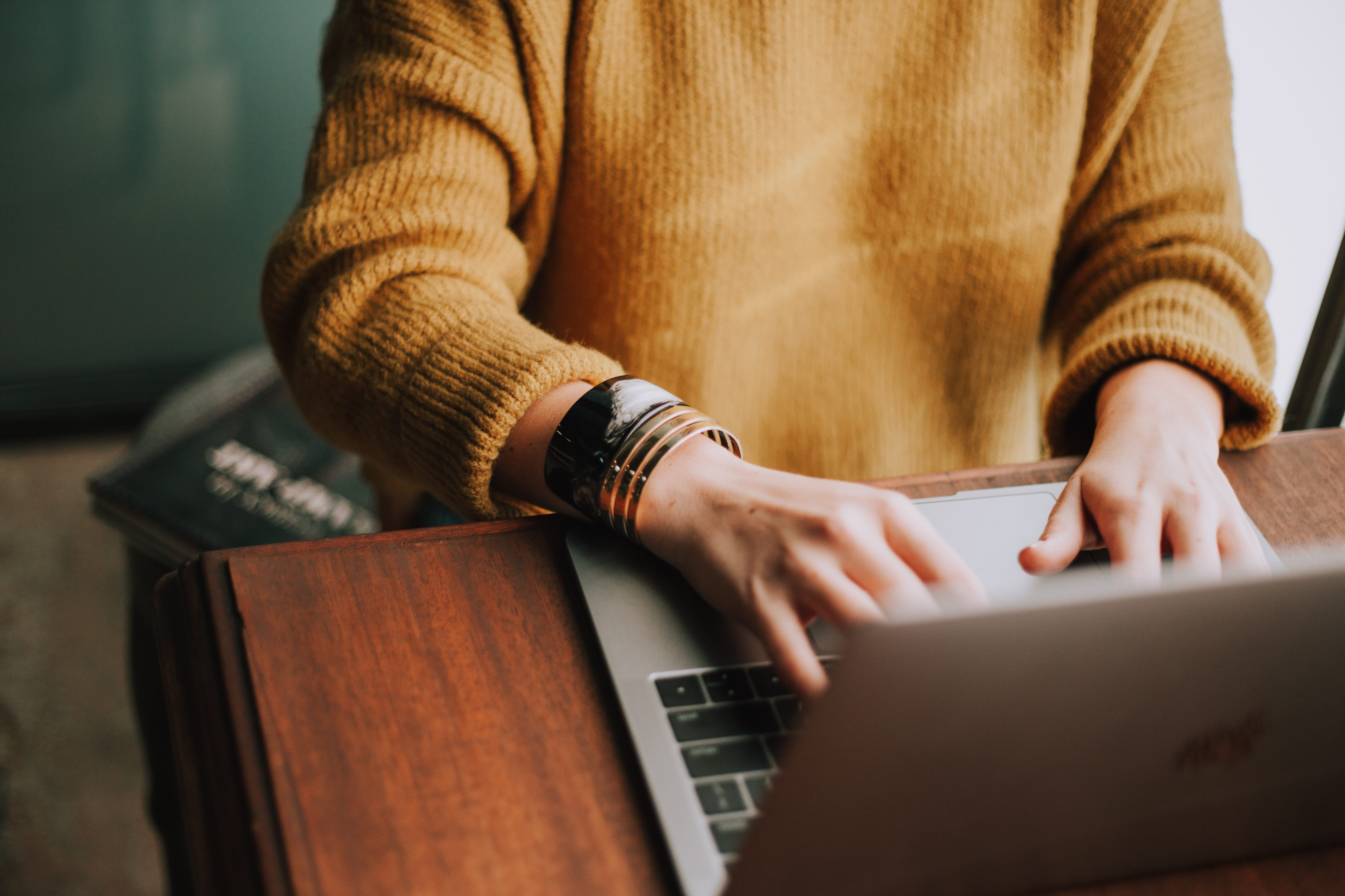 Person in gold sweater using laptop; image by Cristin Hume, via Unsplash.com.