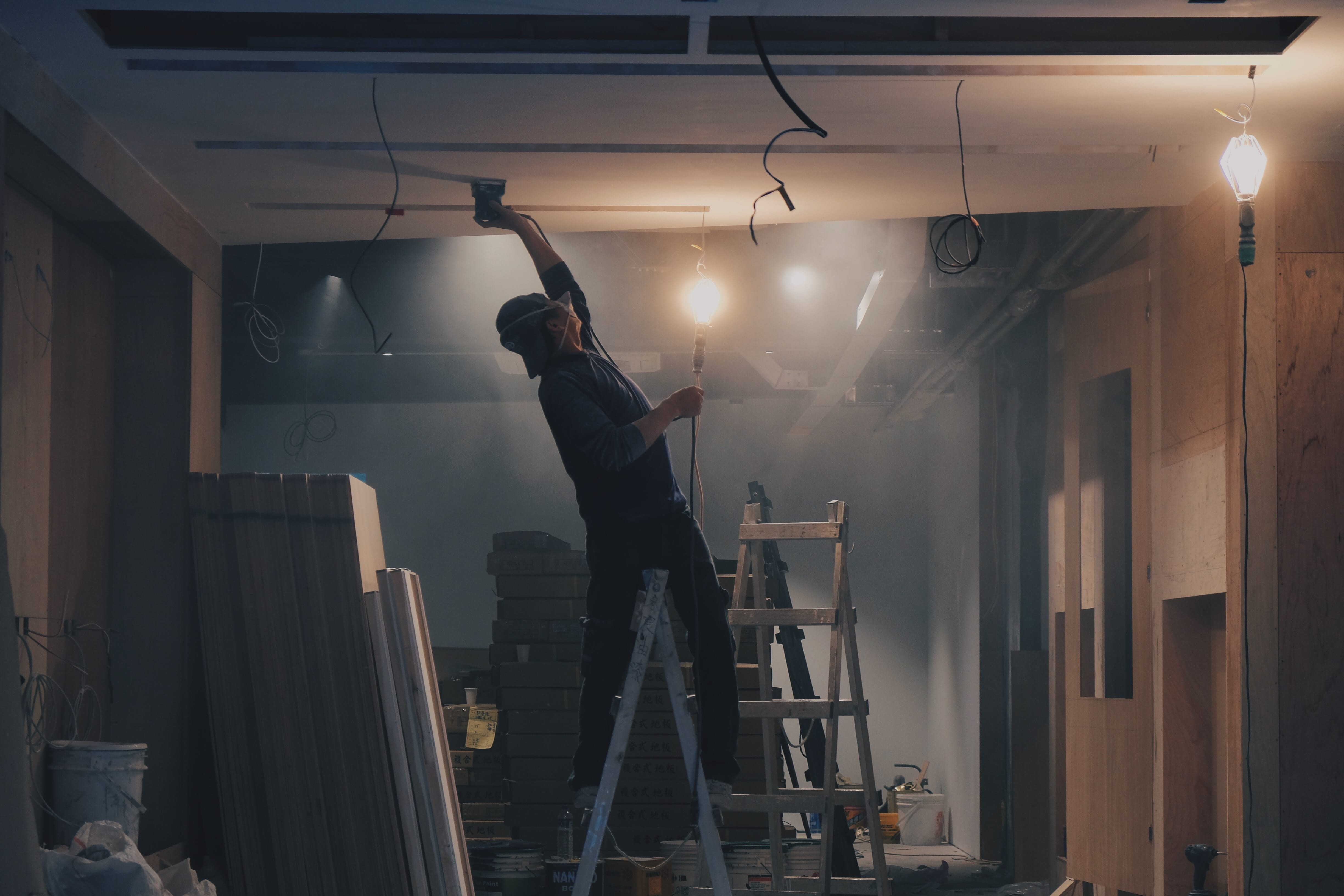 Man on ladder, working on ceiling in construction; image by Henry & Co., via Unsplash.com.