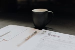 Desk with tax papers, pen, and coffee mug; image by Kelly Sikkema, via Unsplash.com.