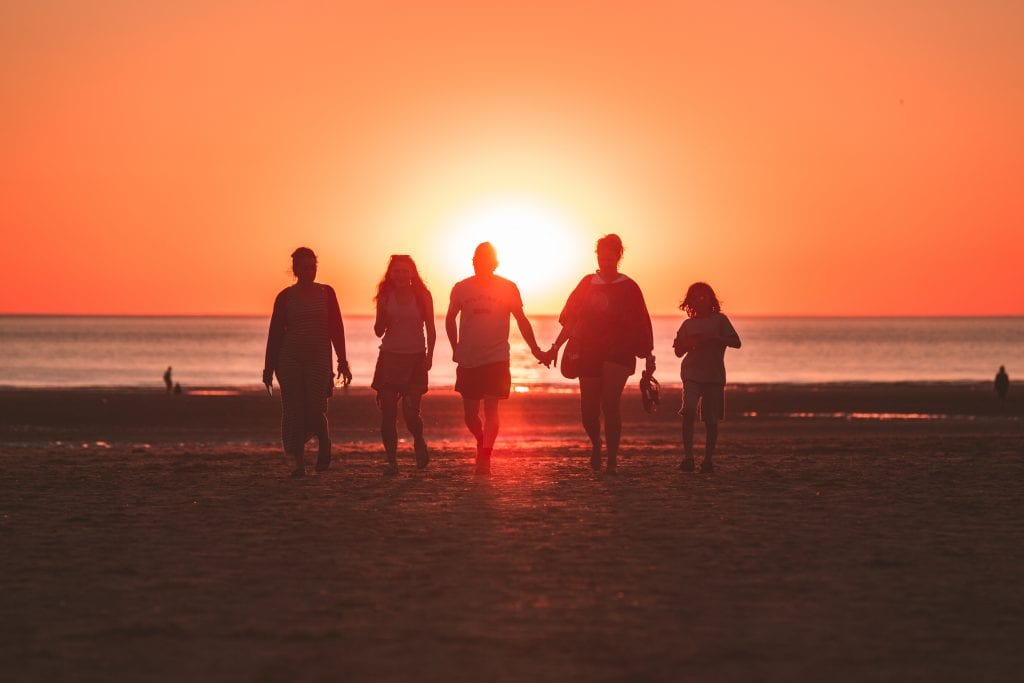 Family of five walking along beach at sunset; image by Kevin Delvecchio, via Unsplash.com.