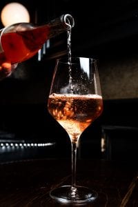 Person pouring pink wine into wine glass; image by Kevin Kelly, via Unsplash.com.