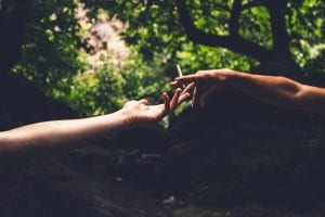 Two people reaching hands toward each other, one holding a joint; image by Louis Hansel, via Unsplash.com.