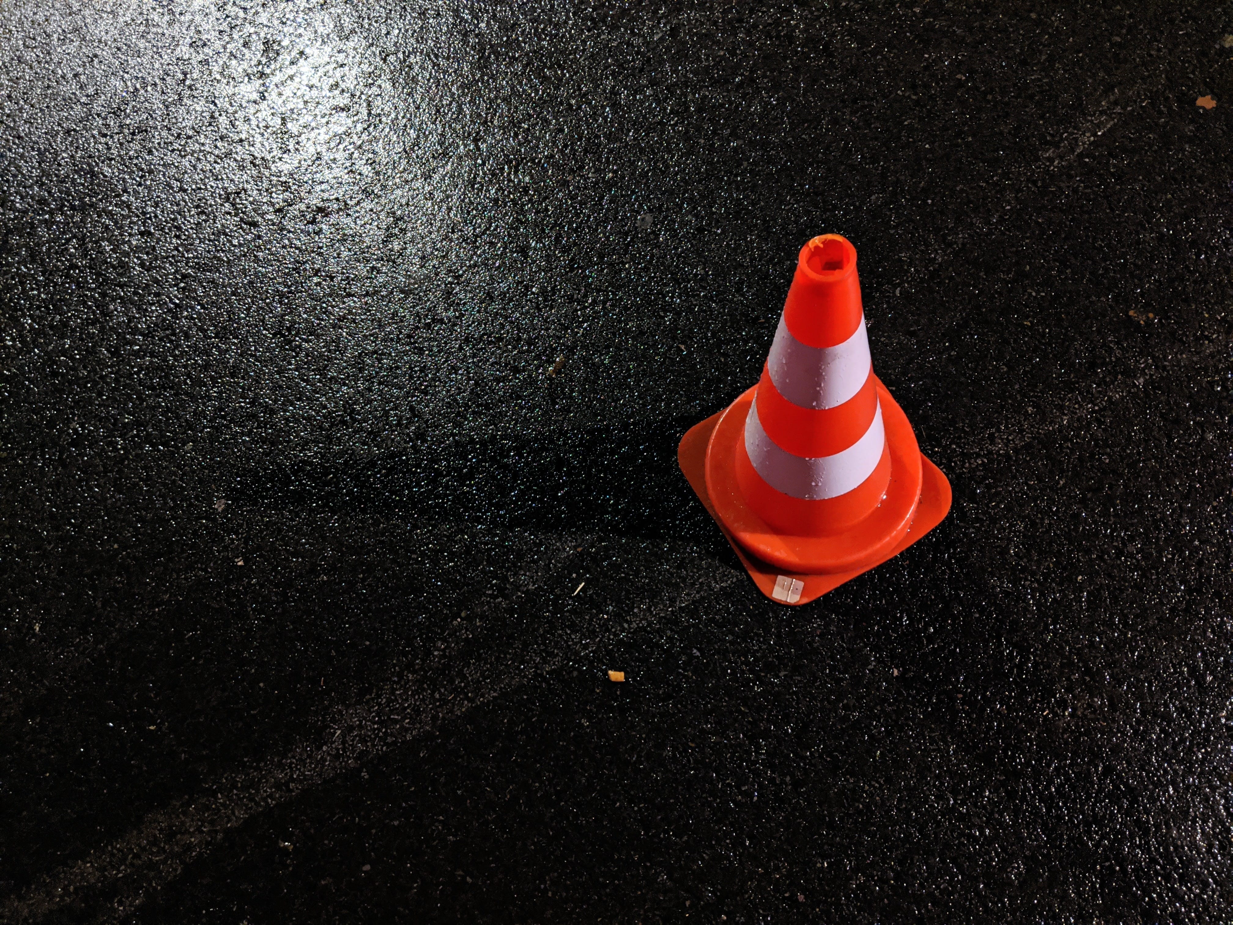 Orange and white traffic cone on dark pavement; image by Lucian Alexe, via Unsplash.com.
