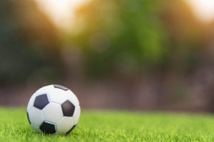 Black and white soccer ball on green field; image by Tevarak Phanduang, via Unsplash.com.