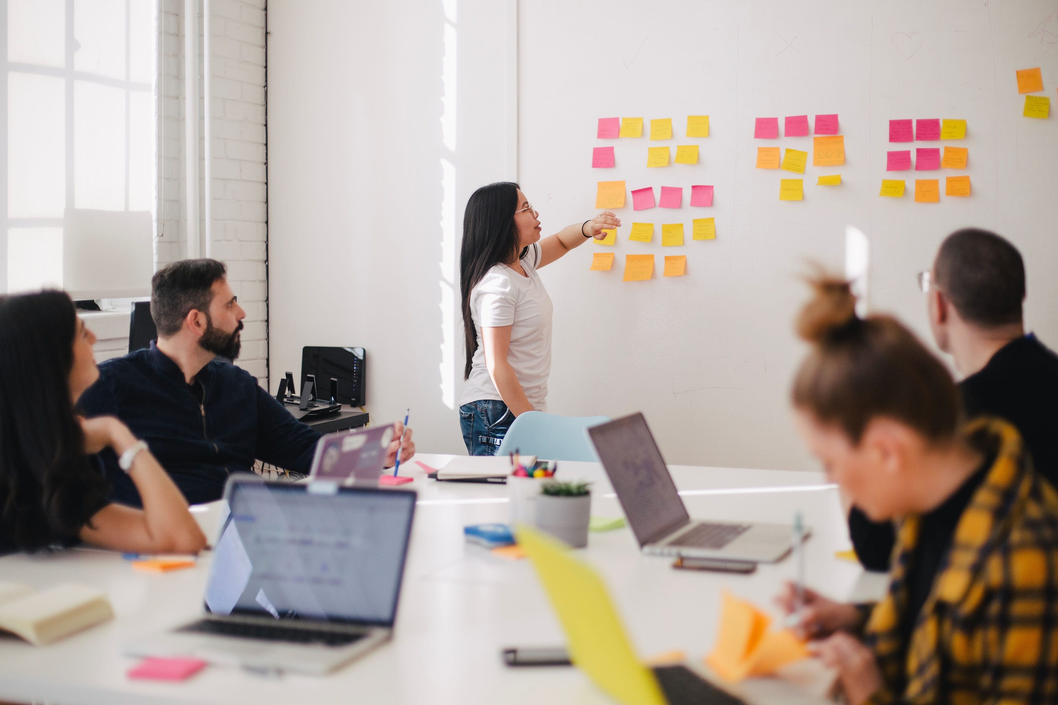 Woman placing sticky notes on the wall during a meeting; image by You X Ventures, via Unsplash.com.