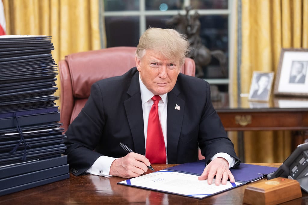 President Trump signing a stack of papers in the Oval Office.