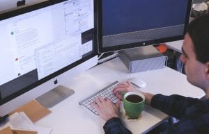 Man working at computer with cup of coffee; image by StartupStockPhotos, via Pixabay.com.