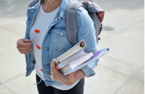 Young female student carrying books, binders, and a backpack; image by Element5 Digital, via Unsplash.com.