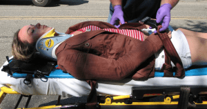 Woman in brown blazer on stretcher with cervical collar; image by Alexisrael, via Wikimedia Commons, CC BY-SA 3.0, no changes.