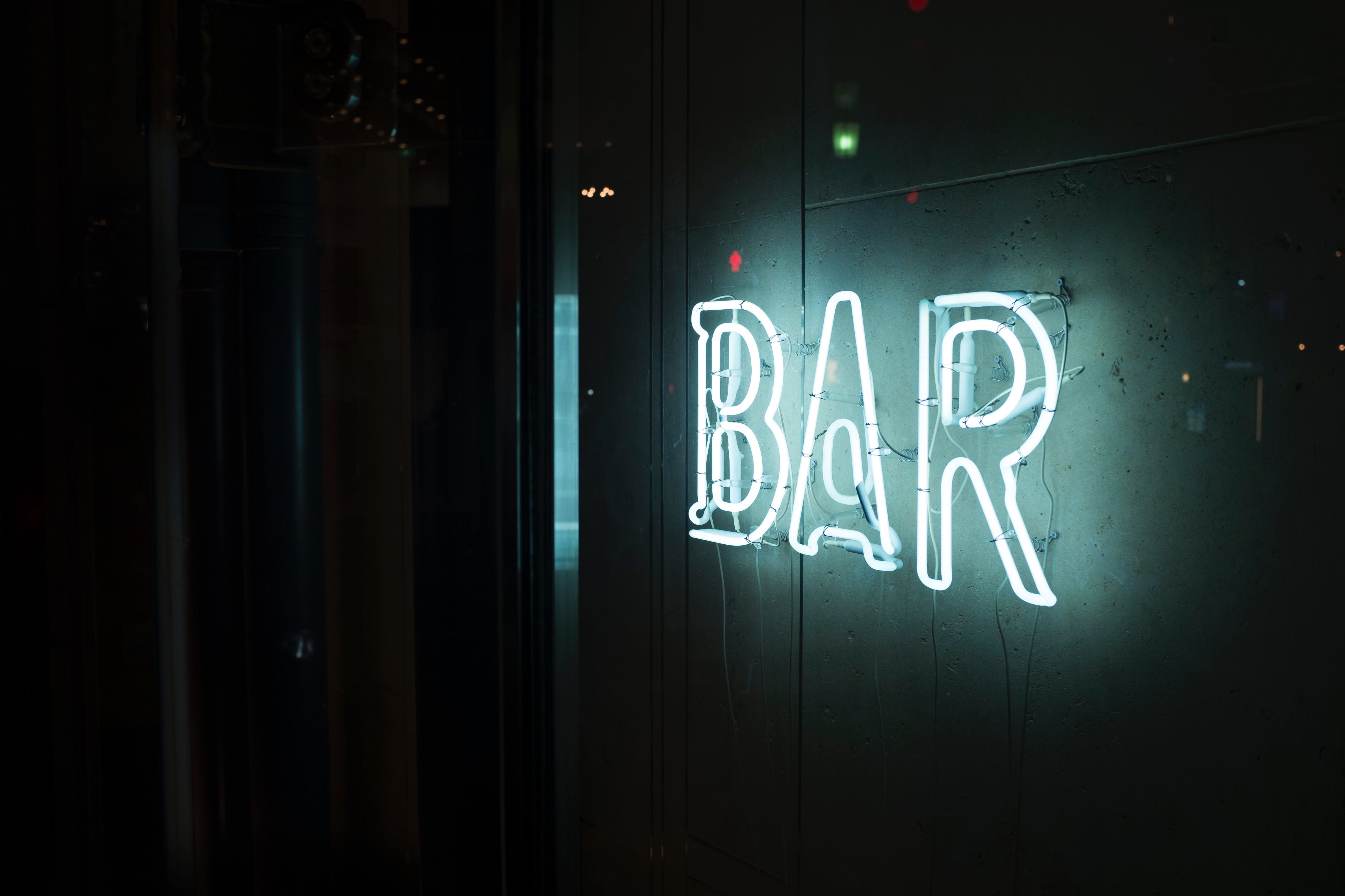 Photo of turned-on white neon sign saying “Bar;” image by Alex Knight, via Unsplash.com.