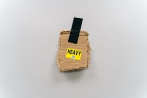 Piece of cardboard with “Heavy” sticker on it taped to neutral wall with black tape; image by Keagan Henman, via Unsplash.com.
