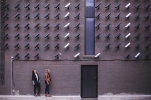 Two women facing security cameras mounted on structure above; image by Matthew Henry, via Unsplash.com.