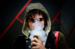 Young man in hoodie vaping; image by Nery Zarate, via Unsplash.com.