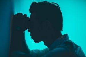 Silhouette of man, forearms against wall & forehead on hands; image by Road Trip with Raj, via Unsplash.com.