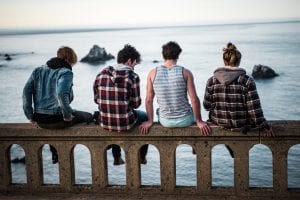 Four teens sitting on bench in front of body of water; image by Sammie Vasquez, via Unsplash.com.