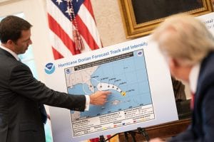 President Trump observes a suit-clad man motioning over a hurricane chart.