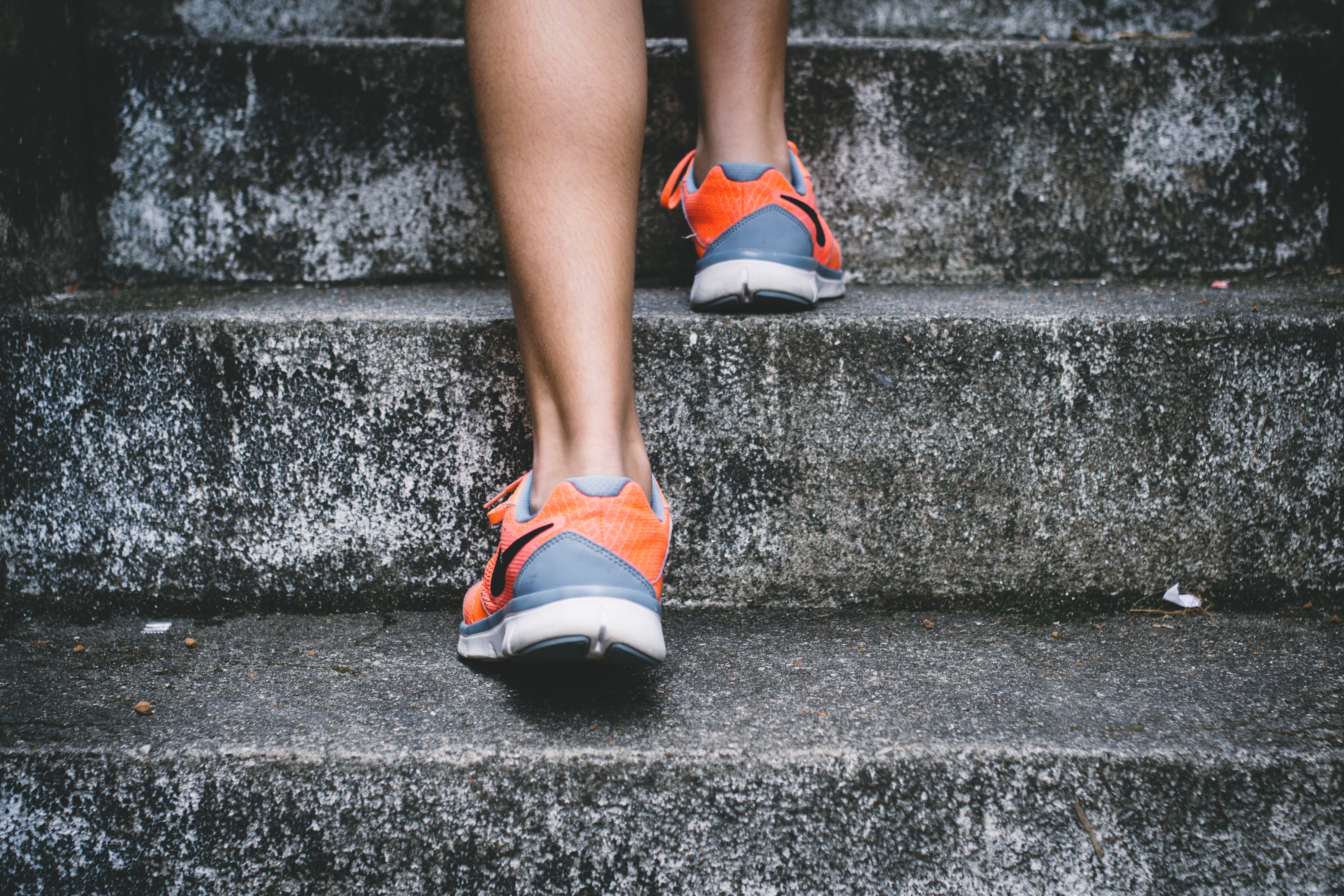 Person wearing orange and gray Nike shoes walking on gray concrete stairs; image by Bruno Nascimento, via Unsplash.com.