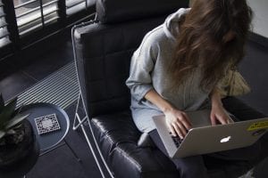 Woman in blue chambray long-sleeved top sitting on black leather chair with silver MacBook on lap; image by Daria Nepriakhina, via Unsplash.com.