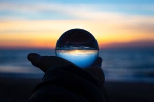 Person holding clear glass ball at sunrise; image by Drew Beamer, via Unsplash.com.