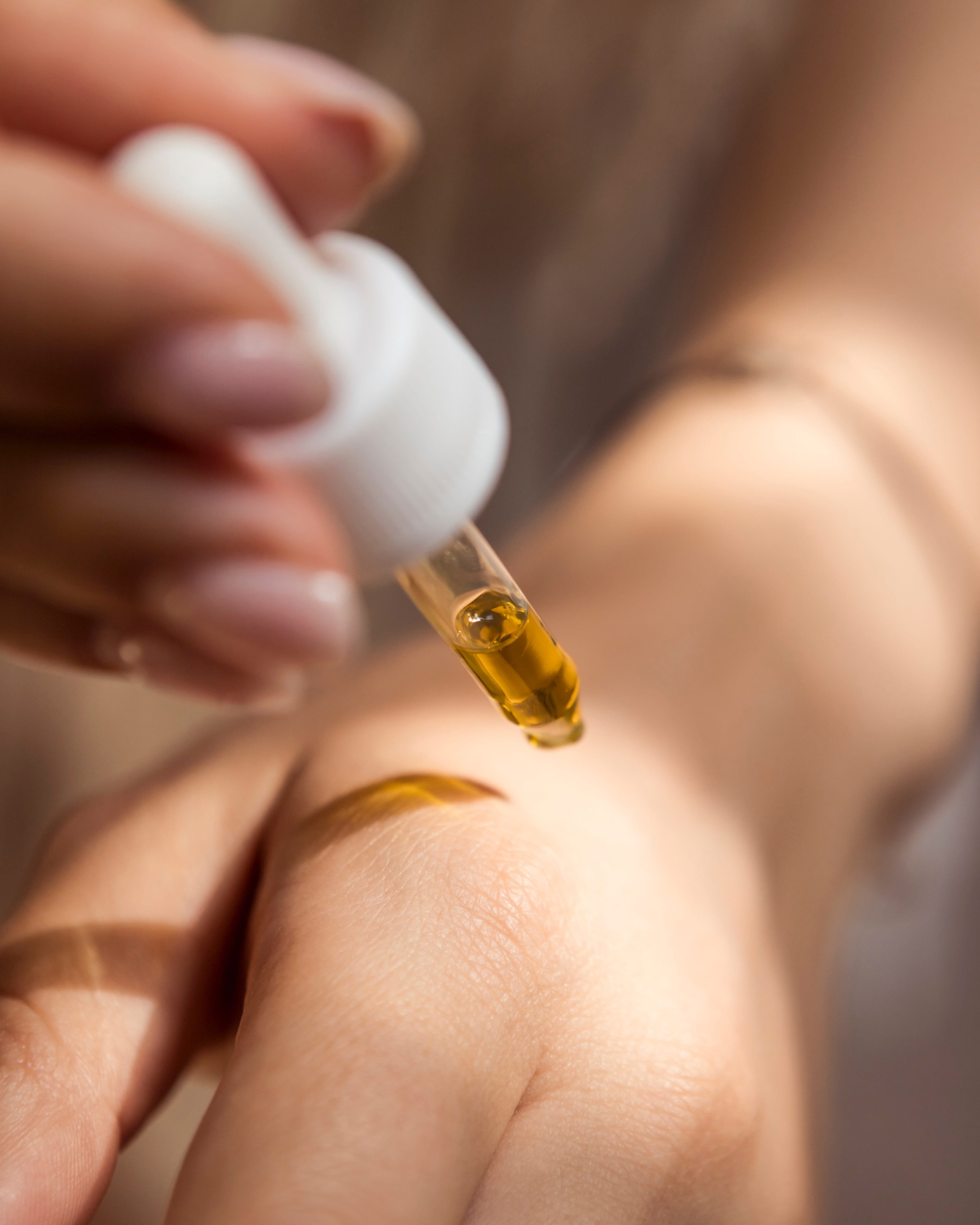 Woman holding dropper of oil over the back of her hand; image by Enecta Cannabis extracts, via Unsplash.com.