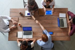 Group of people with laptops having meeting at brown wooden table; image by Fauxels, via Pexels.com.