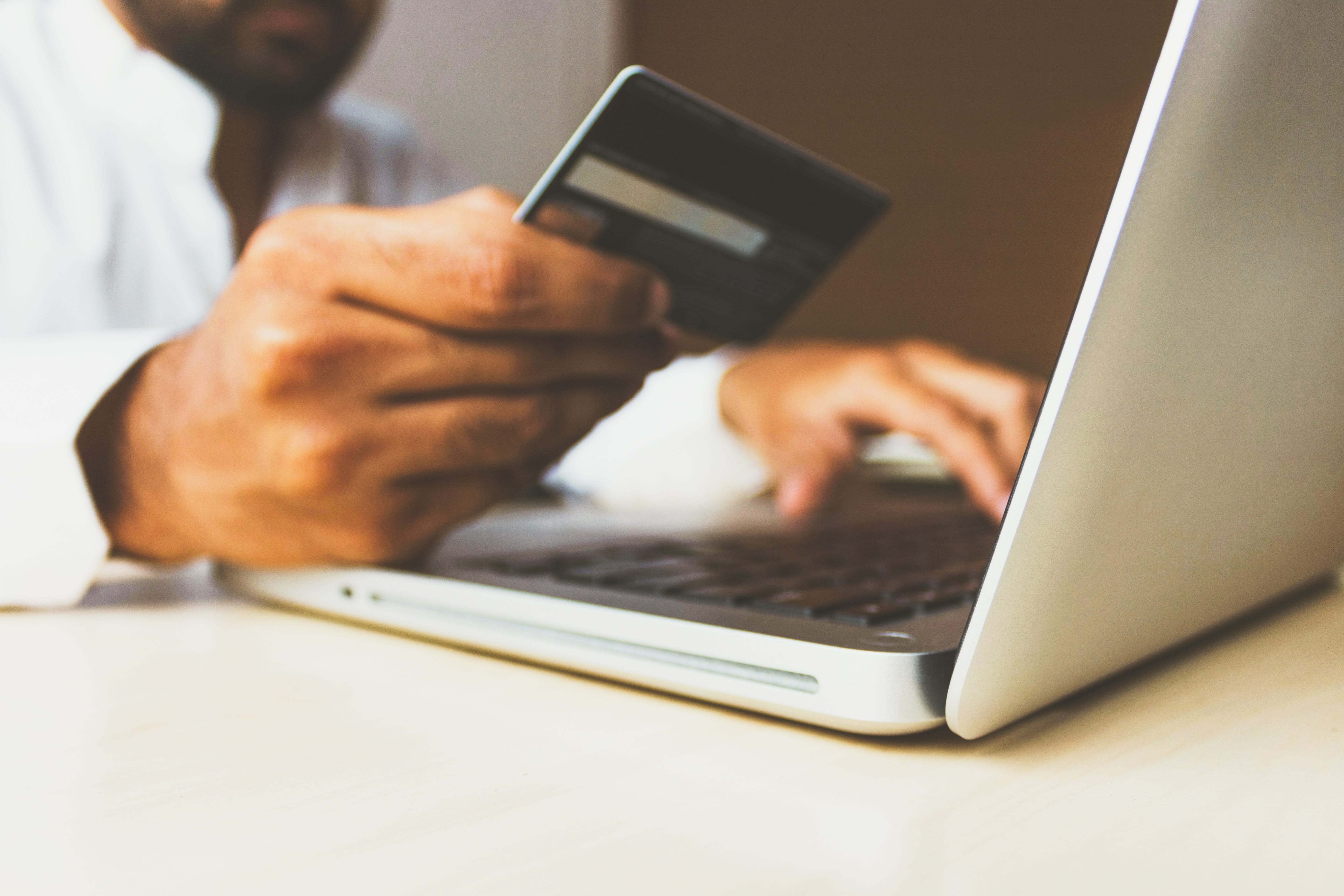 Man holding credit card shopping via laptop; image by rupixen.com, via Unsplash.com.