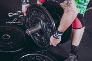 Man holding black Rogue weight plate; image by Victor Freitas, via Unsplash.com.