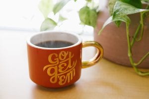 Orange and white ceramic mug with “Go Get ‘Em” written on it near green leaf plant with brown pot; image by Kyle Glenn, via Unsplash.com.