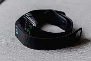 Apple Watch and Fitbit on grey fabric background; image by Andres Urena, via Unsplash.com.