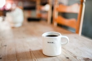 White mug of coffee with “Begin” written on it; image by Danielle MacInnes, via Unsplash.com.