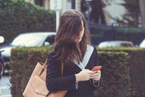 Selective focus photography of woman standing near topiary while holding smartphone; image by Dries De Schepper, via Unsplash.com.