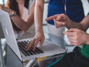 One person touching and another pointing at a MacBook Pro; image by Mimi Thian, via Unsplash.com.