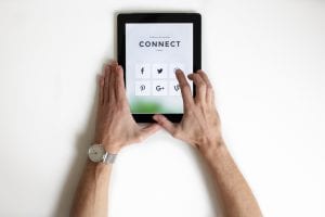 Person using iPad with social media icons onscreen; image by NordWoodThemes, via Unsplash.com.