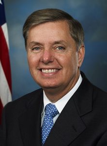 A white man in a suit, backed by the American flag.