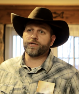 A bearded man in a plaid shirt and cowboy hat.