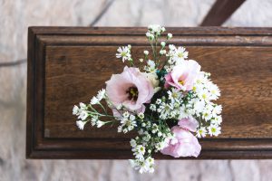 Pink and white flowers on a plain wooden casket; image by Mayron Oliveira, via Unsplash.com.